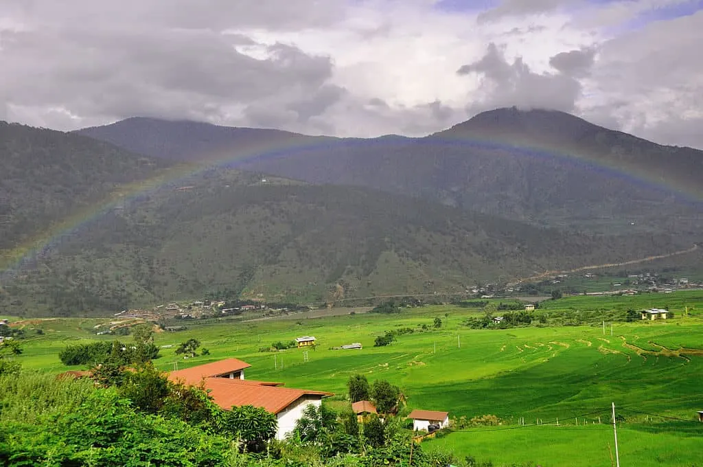 1024px The households in the midst of green paddy field embraced by beautiful rainbow