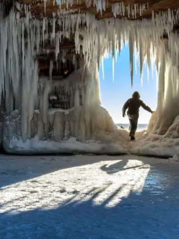 A person steps through an icicle-laden hole in the sandstone formations on Wisconsin's Apostle Islands National Lakeshore near Meyer's beach; Lake Superior.