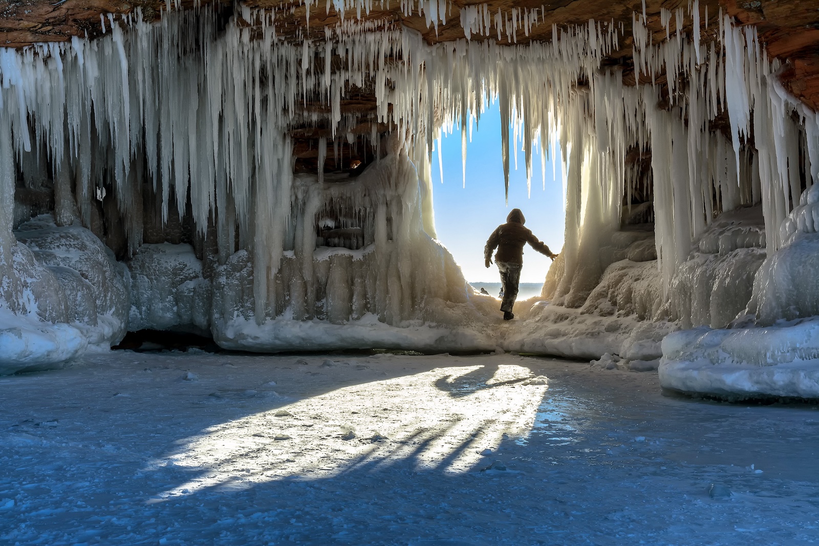 A person steps through an icicle-laden hole in the sandstone formations on Wisconsin's Apostle Islands National Lakeshore near Meyer's beach; Lake Superior.